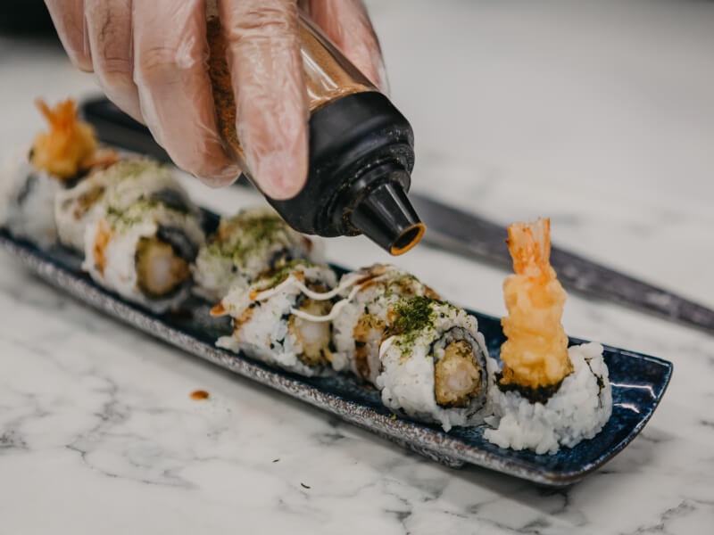 Person seasoning a row of handmade sushi rolls